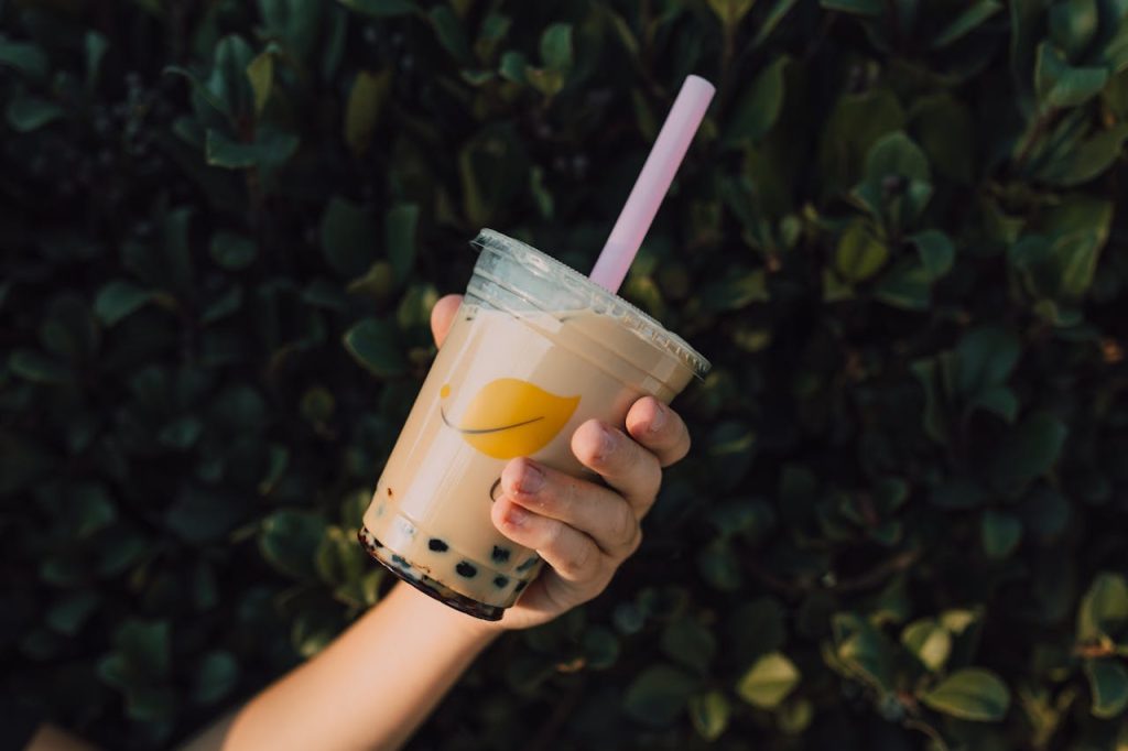 Close-up of a hand holding a refreshing milk tea with boba, outdoors against greenery.
